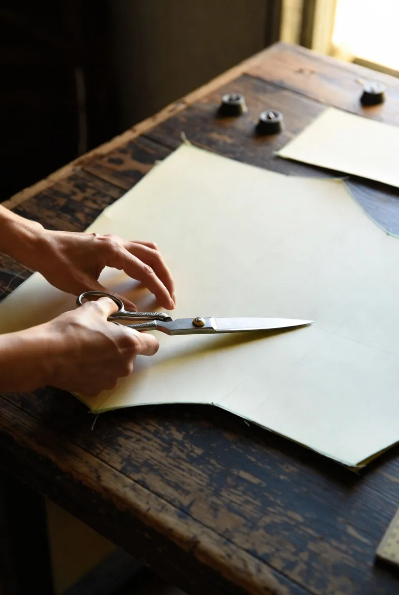 Mani di modellista con forbici artigianali su cartamodello, tavolo da taglio in legno antico